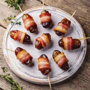Datteln im Speckmantel auf einem Teller – herzhaftes Fingerfood für Partys oder als Vorspeise.